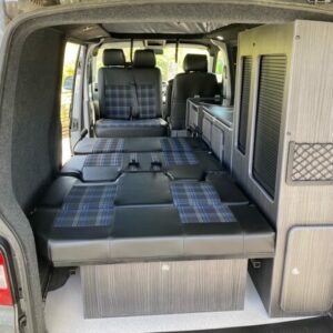 From the open back doors a Dymond Rock and Roll bed l A Dymond Rock and Roll bed inside a camper van trimmed with black and blue check