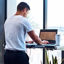 An ergonomic sit stand desk with a man in a white teeshirt